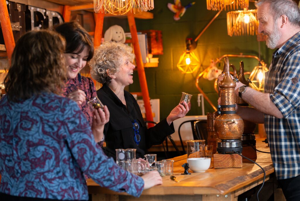 Three women and a man gathered around a tall wooden bench testing different gin flavours.